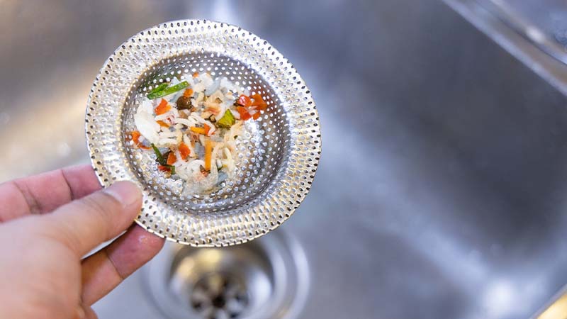 pessoa a segurar proteção do ralo do lava-loiça com restos de comida